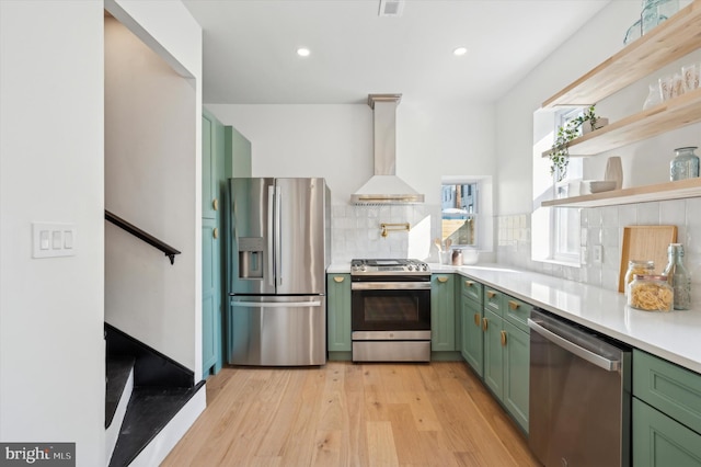 kitchen featuring stainless steel appliances, decorative backsplash, green cabinetry, light hardwood / wood-style flooring, and wall chimney range hood