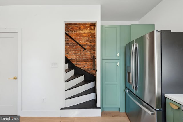 interior space with green cabinets, stainless steel fridge with ice dispenser, and light hardwood / wood-style flooring