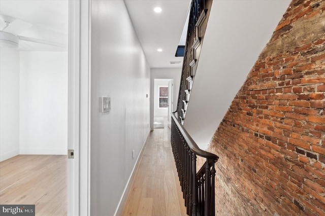 hallway featuring light wood-type flooring and brick wall