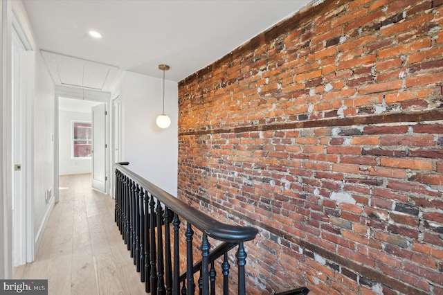 hall with light hardwood / wood-style floors and brick wall