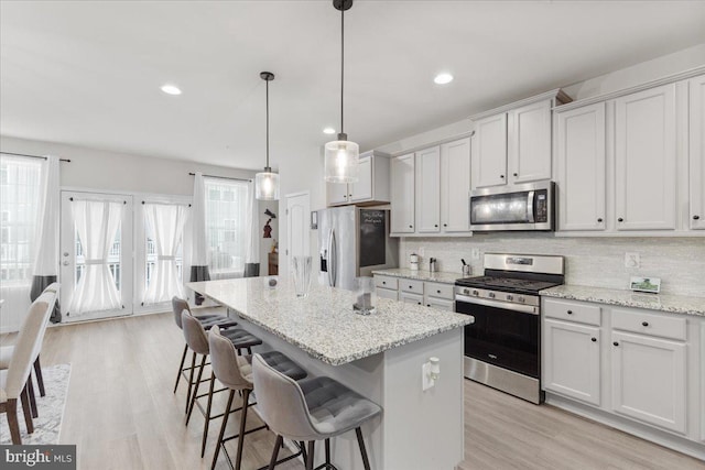 kitchen with stainless steel appliances, tasteful backsplash, light stone countertops, a kitchen island, and decorative light fixtures