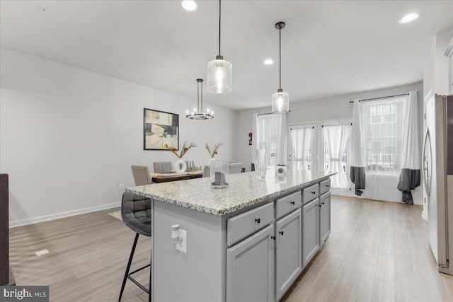 kitchen with pendant lighting, stainless steel refrigerator, gray cabinetry, a center island, and light stone countertops