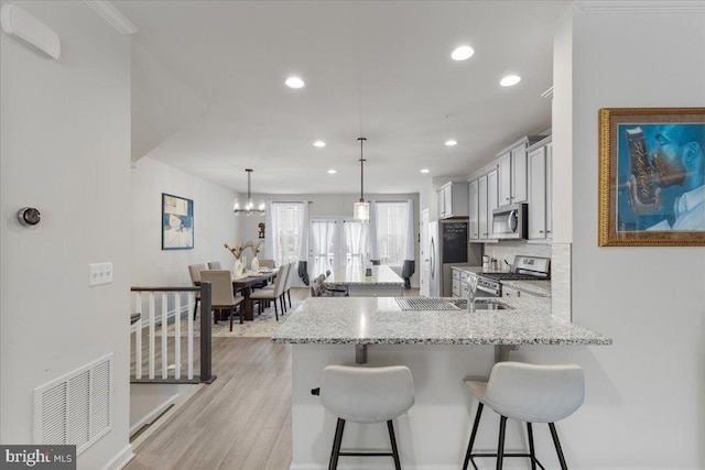 kitchen with appliances with stainless steel finishes, decorative light fixtures, a breakfast bar area, kitchen peninsula, and light stone countertops