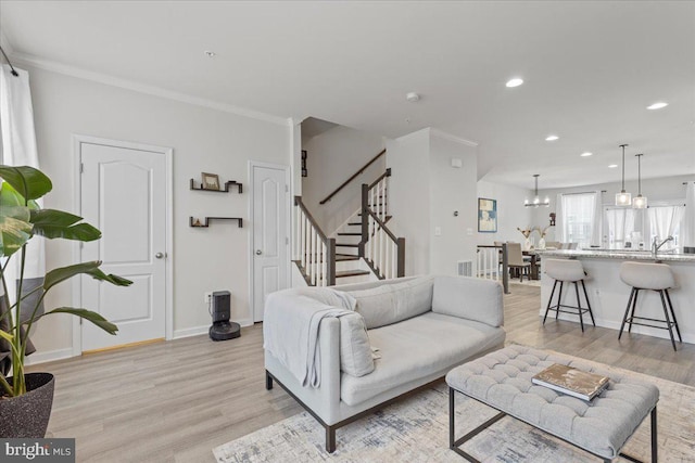 living room featuring sink, ornamental molding, light hardwood / wood-style floors, and a chandelier