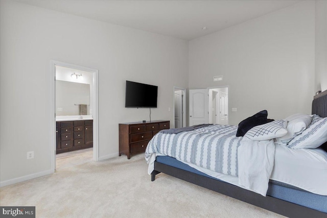 bedroom featuring ensuite bath, light colored carpet, and a high ceiling