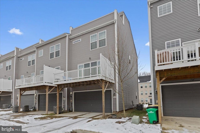 snow covered property featuring a balcony, a garage, and central air condition unit