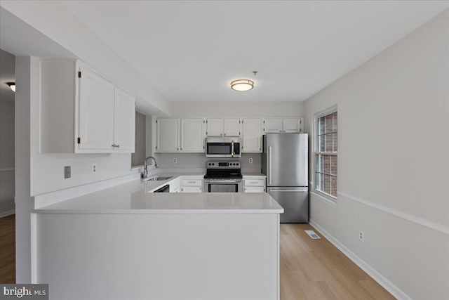 kitchen with a peninsula, visible vents, white cabinets, a sink, and stainless steel appliances