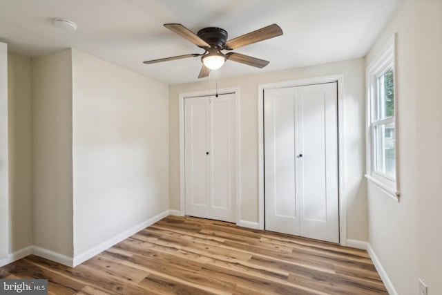 unfurnished bedroom with two closets, ceiling fan, and light wood-type flooring