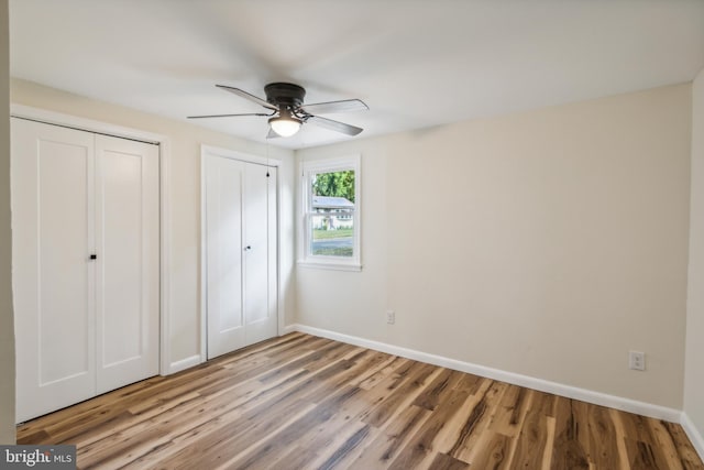 unfurnished bedroom with ceiling fan, two closets, and wood-type flooring