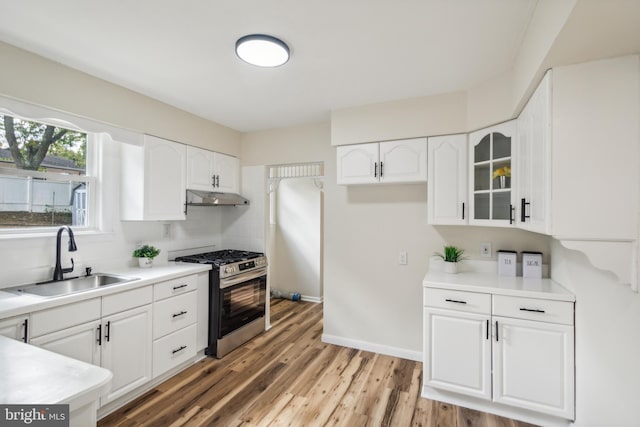 kitchen with white cabinets, light wood-type flooring, stainless steel range with gas cooktop, sink, and tasteful backsplash