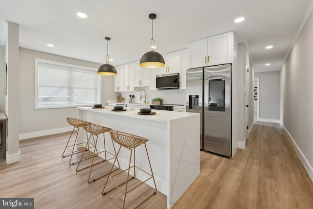 kitchen featuring hanging light fixtures, stainless steel appliances, tasteful backsplash, light wood-type flooring, and white cabinets