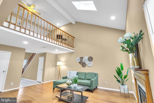 living room with high vaulted ceiling, beam ceiling, a skylight, and light hardwood / wood-style flooring