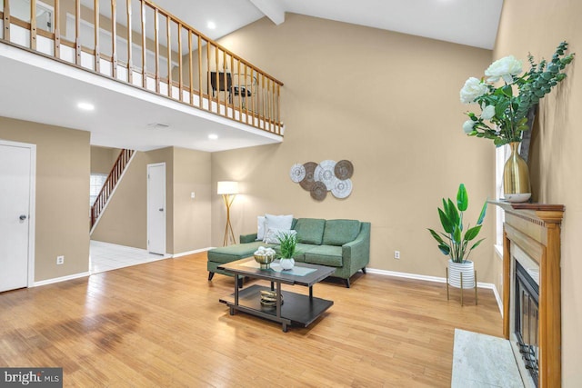 living room featuring hardwood / wood-style flooring, a premium fireplace, high vaulted ceiling, and beam ceiling