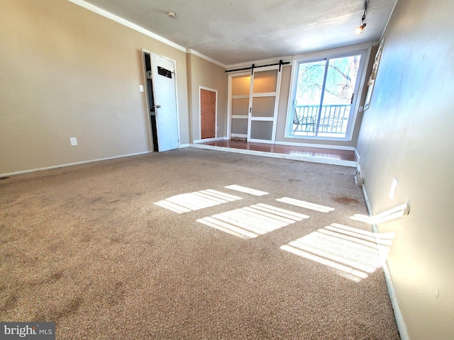 carpeted spare room with track lighting, crown molding, and a barn door