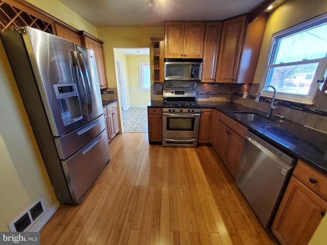 kitchen with stainless steel appliances, light hardwood / wood-style floors, decorative backsplash, dark stone counters, and sink