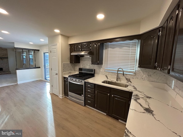 kitchen with a brick fireplace, light hardwood / wood-style floors, sink, stainless steel range with gas stovetop, and dark brown cabinets