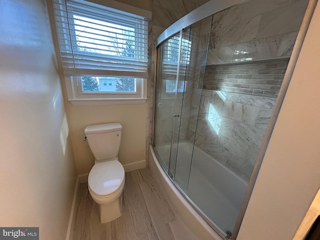 bathroom with wood-type flooring, bath / shower combo with glass door, and toilet