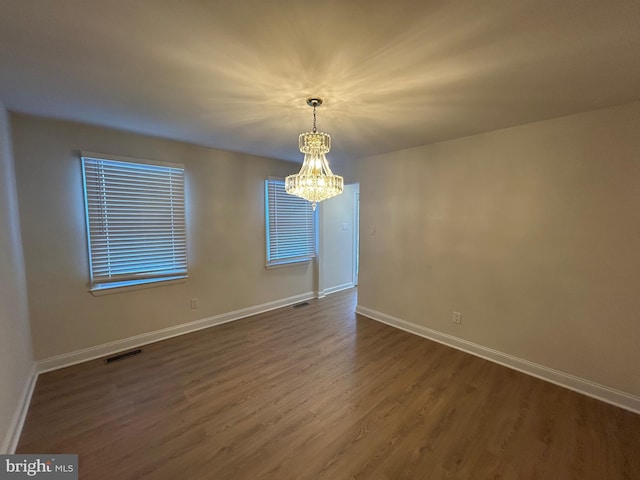 unfurnished room featuring dark wood-type flooring and a notable chandelier