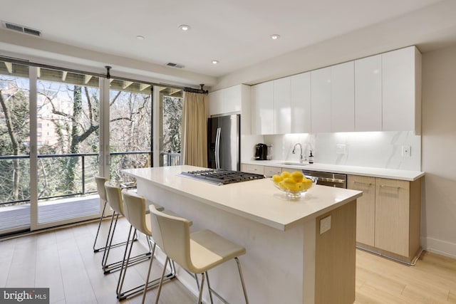 kitchen with appliances with stainless steel finishes, a kitchen island, sink, white cabinetry, and tasteful backsplash