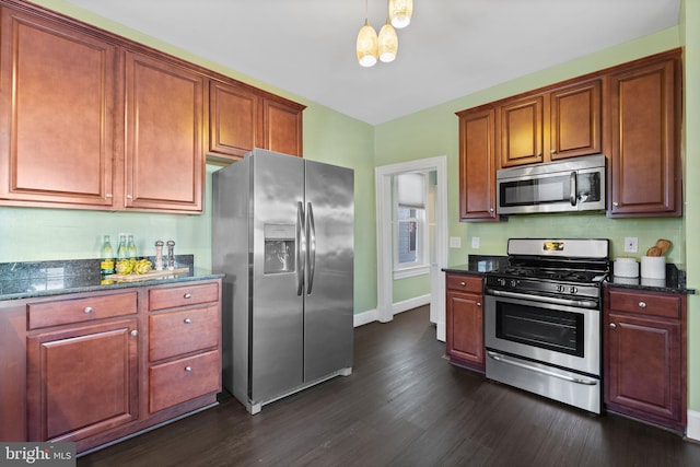 kitchen with decorative light fixtures, stainless steel appliances, dark wood-type flooring, and dark stone countertops