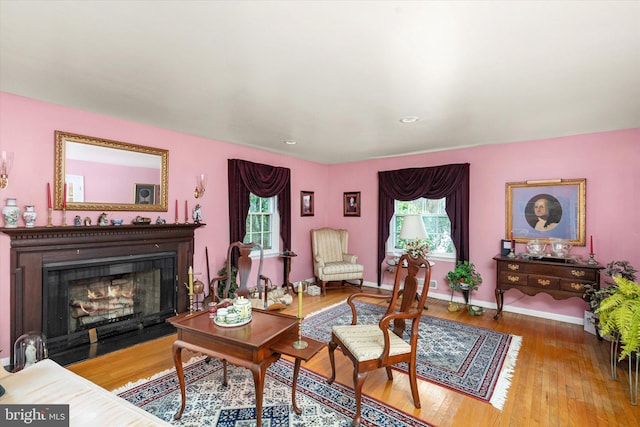 living area featuring a fireplace with flush hearth, wood-type flooring, and baseboards