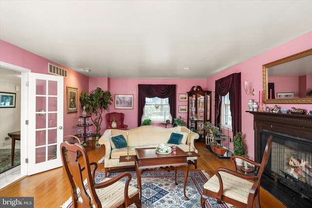 living area with french doors, visible vents, a lit fireplace, and wood finished floors