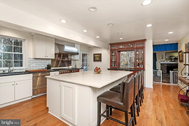 kitchen featuring wall chimney exhaust hood, light wood finished floors, a kitchen island, and a sink