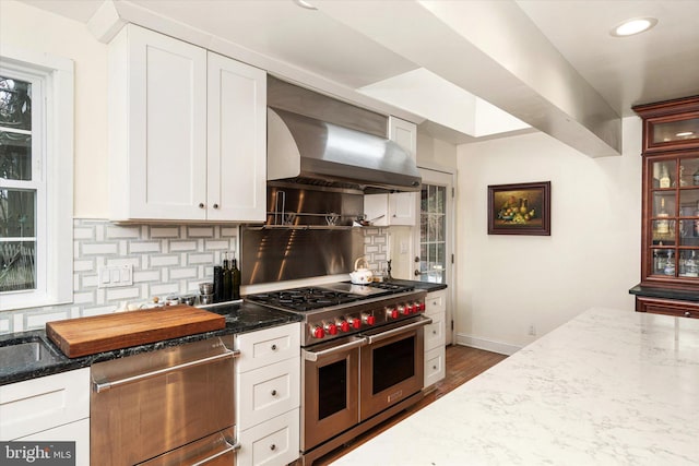 kitchen featuring tasteful backsplash, white cabinets, dark stone counters, appliances with stainless steel finishes, and wall chimney range hood