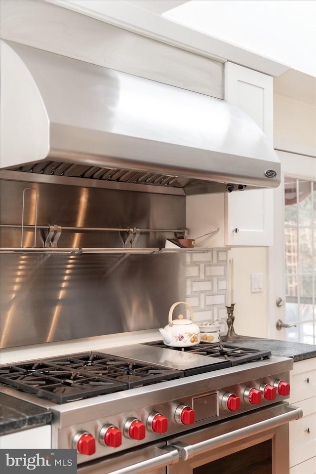 kitchen with decorative backsplash, dark countertops, wall chimney range hood, double oven range, and white cabinetry