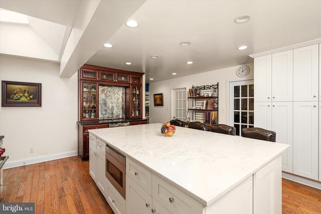 kitchen featuring a kitchen island, stainless steel microwave, glass insert cabinets, light wood-type flooring, and recessed lighting