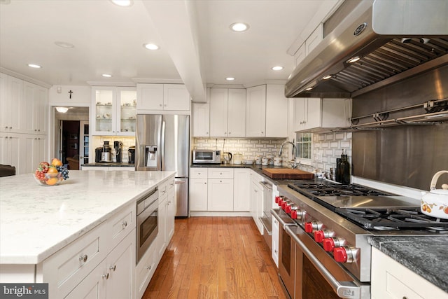 kitchen with stainless steel appliances, white cabinetry, light wood-style floors, and ventilation hood