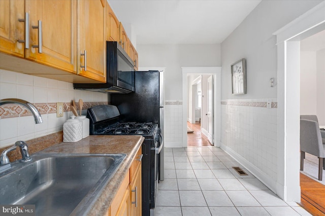 kitchen with sink, tile walls, light tile patterned floors, and black appliances