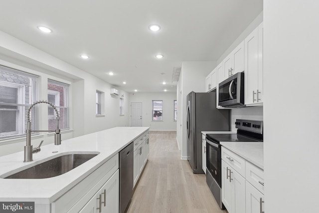 kitchen featuring an AC wall unit, white cabinets, appliances with stainless steel finishes, light hardwood / wood-style floors, and sink