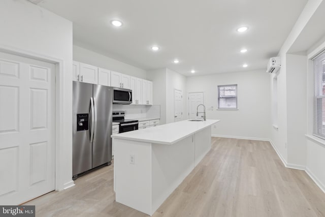 kitchen with appliances with stainless steel finishes, sink, light wood-type flooring, white cabinetry, and a kitchen island with sink