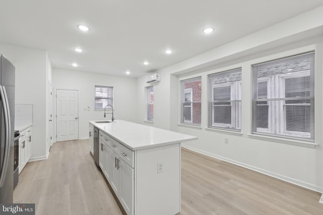 kitchen featuring light hardwood / wood-style flooring, sink, white cabinetry, a center island with sink, and stainless steel appliances