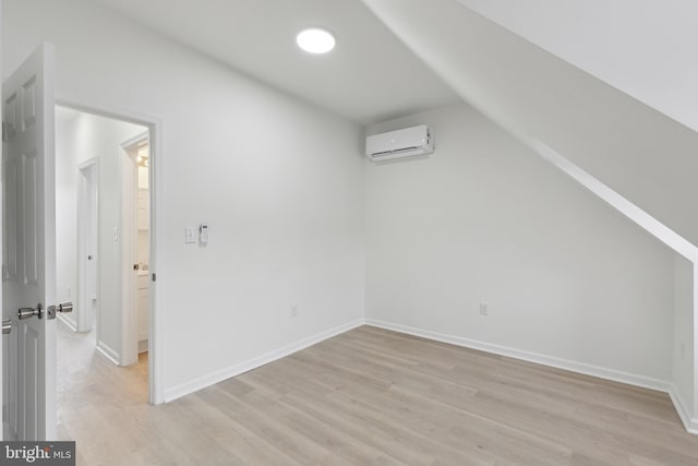 additional living space featuring light hardwood / wood-style floors, vaulted ceiling, and an AC wall unit