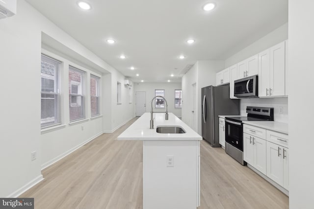 kitchen featuring light hardwood / wood-style floors, appliances with stainless steel finishes, white cabinetry, sink, and an island with sink