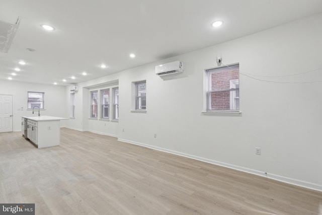 unfurnished living room with an AC wall unit, sink, and light wood-type flooring