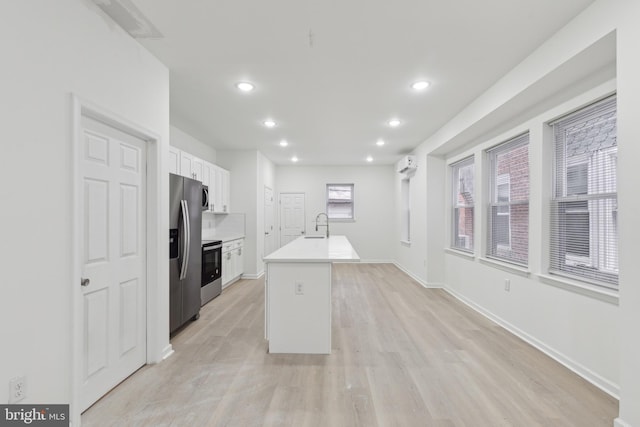 kitchen with sink, white cabinetry, an AC wall unit, a center island with sink, and stainless steel appliances