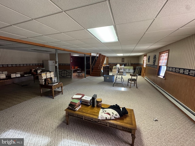 interior space featuring a paneled ceiling, wooden walls, and a baseboard heating unit