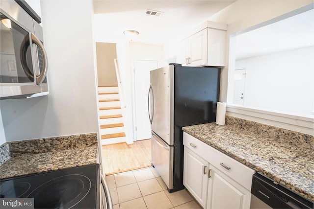 kitchen with white cabinets, stainless steel appliances, stone countertops, and light tile patterned flooring