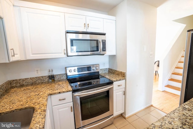 kitchen with white cabinets, stainless steel appliances, stone counters, and light tile patterned flooring