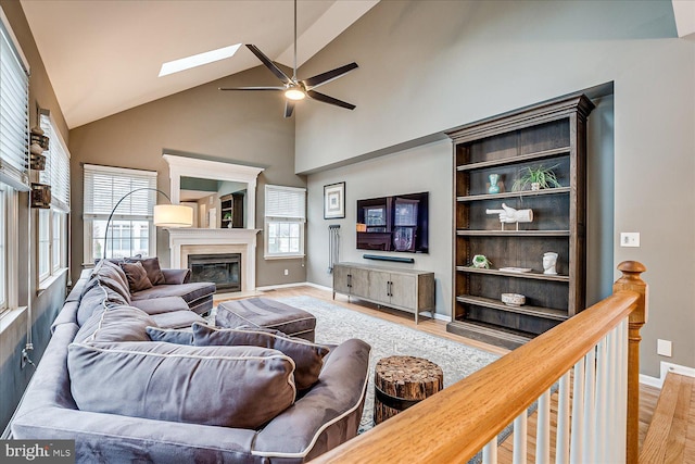 living room featuring light wood-type flooring, ceiling fan, and lofted ceiling with skylight