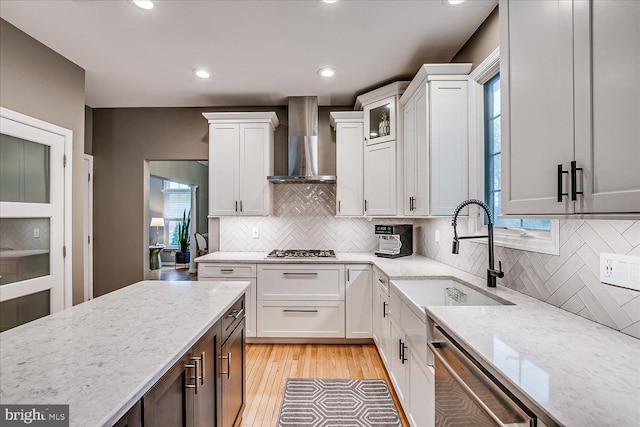 kitchen featuring sink, white cabinets, light stone countertops, wall chimney range hood, and stainless steel appliances