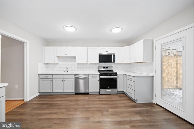 kitchen featuring stainless steel appliances, sink, white cabinetry, wood-type flooring, and decorative backsplash