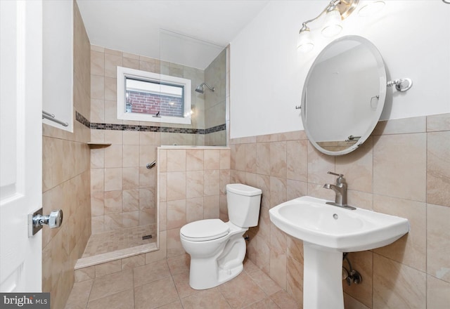 bathroom featuring toilet, tile patterned flooring, tiled shower, and tile walls