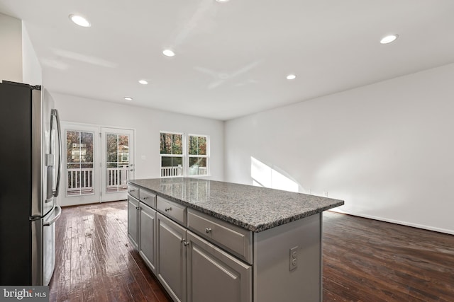 kitchen with a center island, stainless steel refrigerator with ice dispenser, dark hardwood / wood-style flooring, gray cabinetry, and dark stone countertops