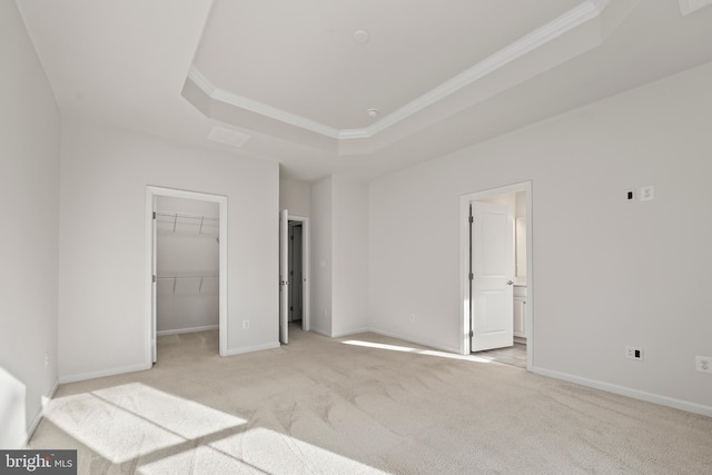 unfurnished bedroom featuring light colored carpet, crown molding, a spacious closet, a tray ceiling, and ensuite bathroom