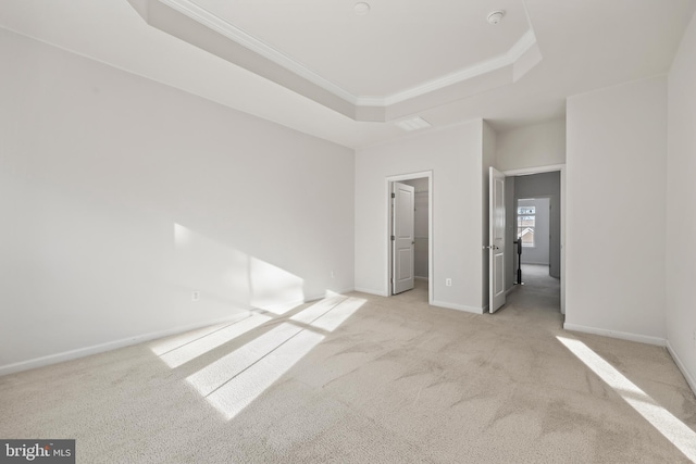 unfurnished bedroom featuring ornamental molding, a walk in closet, light carpet, and a raised ceiling