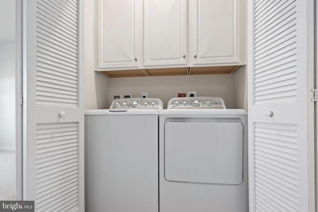 clothes washing area with washing machine and clothes dryer and cabinets